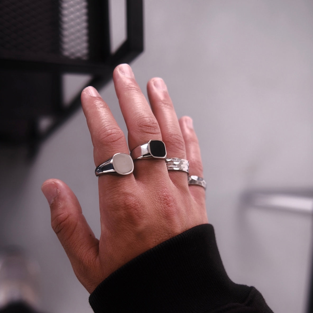 Mens hand with silver rings on, including a signet ring with black stone, a plain signet and a hammered band ring